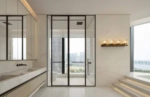Modern luxury bathroom with white marble walls and double vanity, black-framed glass shower, freestanding tub, and large windows revealing a city skyline and river view.