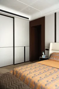 Contemporary bedroom interior with dark walnut built-in wardrobe, textured light grey walls, cream leather headboard, and orange and grey geometric patterned bedding on a low platform bed.