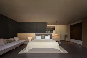 Modern minimalist bedroom featuring a large dark slate stone feature wall, built-in daybed with neutral cushions, king size bed with white linens, pendant light, and large abstract painting.