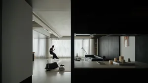 Modern minimalist living room featuring a hanging indoor swing, micro-cement walls and ceiling, dark wood paneling, and a black leather sofa under soft natural light.