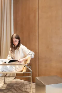 Woman with long brown hair reading a book while seated in a modern chrome and leather chair against a warm wood-paneled wall