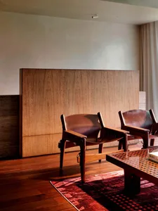 Mid-century modern living room featuring two rosewood and leather sling chairs, a large rosewood room divider, dark wood flooring, and a red patterned area rug.