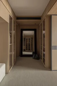 Narrow walk-in closet featuring light oak wood cabinetry with glass doors, beige carpet flooring, and a large black-framed mirror reflecting another closet space.
