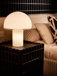 Close-up of a modern white mushroom table lamp on a dark oak grid-patterned bedside table, with neutral textured pillows and woven bedding in the background.