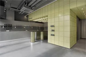 現代材質展示間內部，設有大型萊姆綠穿孔板牆面、混凝土地板、圓柱形金屬展示桌，以及線性LED燈光照明的產品陳列架。
