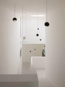 Modern minimalist double-height staircase with white plaster walls and multiple black spherical pendant lights hanging at different heights.