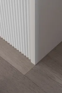 Close-up view of a white fluted baseboard meeting a grey-brown wood laminate floor at a clean 90-degree angle.