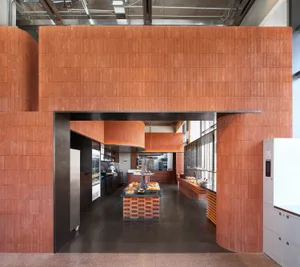 Modern bakery interior featuring extensive terracotta tile walls, a central wooden display island, dark concrete floor, and industrial ceiling with exposed ductwork.