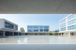 Modern minimalist concrete building complex surrounding a large shallow reflecting pool in a spacious courtyard under bright daylight