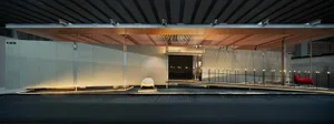 Modern airport lounge interior at night with a large wooden slatted canopy, linear LED lighting, white concrete walls, and red and white sculptural seating.