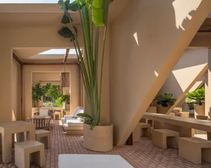 Open-air courtyard lounge featuring raw concrete stools, benches, and large planters with tall tropical plants under a bright skylight.