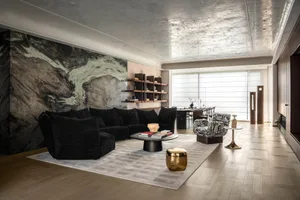 Modern luxury living room featuring a large dramatic green marble wall, black velvet modular sofa, patterned accent chairs, round black coffee table, and metallic ceiling.