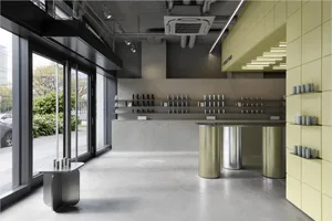 現代極簡零售店內部，擁有拋光混凝土地板、紋理混凝土牆面、不鏽鋼圓柱形櫃檯，以及明亮的萊姆綠穿孔磁磚牆與嵌入式層架。