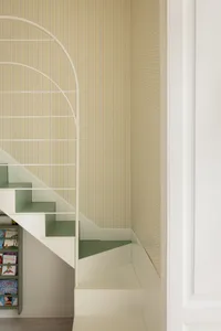 View of a modern children's staircase with sage green steps, white railing, and colorful polka dot wallpaper on the wall, with built-in bookshelf underneath.