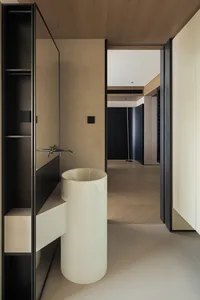 Modern minimalist powder room with a white cylindrical vessel sink, matte black fixtures, oak herringbone flooring, and neutral beige walls.