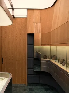 Luxury jewelry boutique interior featuring curved walnut wood paneling, dark green marble floor tiles, and illuminated glass display cases with jewelry.