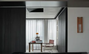 Modern home office nook featuring dark wood walls, a blue-topped vintage desk with orange lamp and red rotary phone, paired with a red leather and chrome director’s chair, white built-in shelving, and a wooden wall clock.