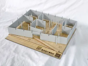 Architectural scale model of an interior space with white partition walls, wooden base, and laser-cut furniture layouts, displayed on a white fabric background.