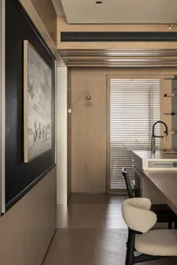 Modern minimalist kitchen featuring light oak cabinetry, black accents, boucle bar stools, and a large framed landscape photograph on a dark wood wall panel.