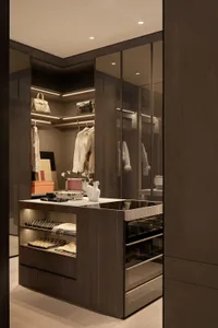 Modern luxury walk-in closet with dark smoked oak cabinetry, white marble-topped central island with built-in drawers and open shelving displaying folded scarves, white ceramic vases, and luxury handbags on backlit upper shelves.