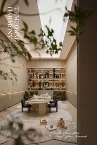 Modern family reading nook featuring two olive-green velvet armchairs, a round marble dining table, built-in backlit shelving filled with books and toys, and a large skylight overhead.