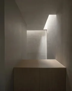 A minimalist architectural alcove with smooth concrete walls and ceiling, featuring a warm oak wood cabinet at the base, illuminated by a dramatic skylight slit.