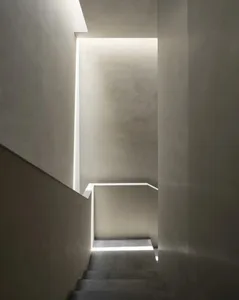 View looking down a minimalist concrete staircase illuminated by continuous linear LED light strips recessed into the walls and ceiling.