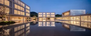 Modern minimalist architecture complex with extensive reflecting pool at dusk, showing perfect symmetry and warm interior lighting.