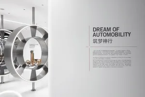 Large circular stainless steel installation with illuminated rings displaying a wooden early automobile model inside, next to a wall panel titled 'Dream of Automobility' in an art gallery.