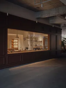 Modern naturalist retail interior with dark wood paneling, illuminated glass display window, and concrete ceiling with pendant lights.