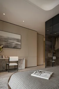 Modern minimalist bedroom interior with marble vanity desk, white upholstered chair, large monochrome ocean photograph, and glass wardrobe in neutral beige tones.
