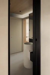 Modern minimalist bathroom featuring a cylindrical white porcelain sink with black floating vanity, viewed through a dark door frame with wood ceiling and neutral walls.