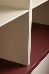 Close-up of modern built-in shelving showing cream painted shelves supported by a thick burgundy painted baseboard.
