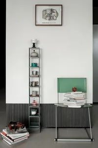 Modern minimalist entryway featuring a tall grey metal shelving unit displaying vintage objects, a bright green leather chair with stacked books, and a framed architectural floor plan labeled 'DREAM HOUSE' on a white wall with dark wood wainscoting.