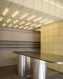 Modern reception desk featuring a curved dark countertop supported by cylindrical stainless steel bases, set against pale yellow perforated wall and ceiling panels with integrated linear lighting.