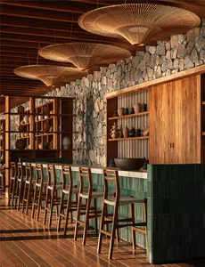 Rustic modern bar interior featuring a long counter with green tile base, wooden bar stools, stone wall, open wooden shelving displaying pottery, and large woven rattan pendant lights hanging from a wood ceiling.