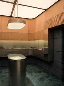 Interior of a luxury jewelry store with curved walnut wood paneling, dark green marble tiled floor, central cylindrical glass display island, and large circular pendant light.