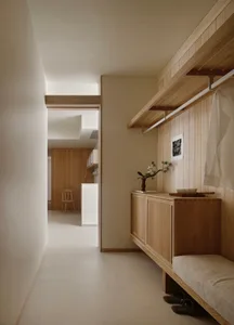 Modern minimalist entryway with light oak built-in bench, upper hanging rod, cabinet storage, and a view into a bright kitchen area.
