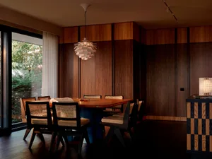 Modern dining room featuring rich walnut wood paneling, a large live-edge dining table, six dark wood cane-back chairs, and a white PH Artichoke pendant lamp hanging above the table.