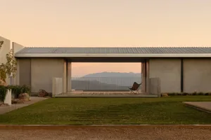 Modern concrete house with open patio, butterfly chair, wooden deck, and distant mountain range at sunset