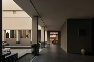 Modern minimalist courtyard featuring a shallow water channel, concrete pillars with black lattice bases, built-in stone seating, and a large ceramic jar against a dark wall.