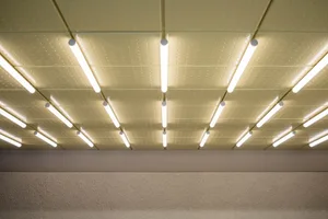 View looking up at a modern ceiling featuring a grid of perforated metal panels and multiple parallel linear LED light fixtures emitting warm white light.