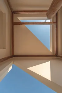 Low-angle architectural view looking up at intersecting wooden beams framing a bright blue sky through a geometric skylight opening.