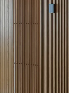 Close-up of a vertical oak wood slat wall featuring two horizontal bands of darker joinery and a modern rectangular blue wall sconce mounted on the upper right.