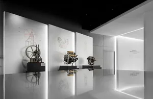Modern exhibition hall with polished reflective floor displaying vintage and modern car engines on black pedestals, backlit technical drawings of mechanical parts on white walls, and signage for Automobile Technology Evolution.