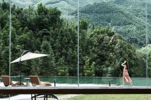 Modern infinity pool with wooden lounge chairs and a large umbrella, set against a dramatic backdrop of dense green mountains and forest in Taiwan.