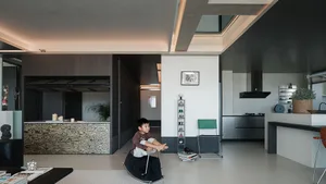 Modern open-plan living and kitchen area with dark wood grain feature wall, concrete ceiling details, and a child playing on a rocking horse.