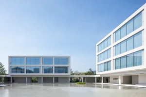 Modern two-story concrete and glass courtyard house with a large reflecting pool in the foreground under a bright blue sky.