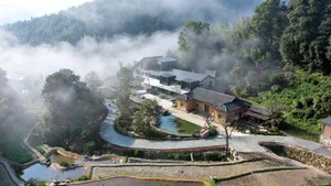 航拍山區度假村，結合現代與傳統中式建築，環繞茂密森林、石砌擋土牆、蜿蜒步道與晨霧籠罩的反射池塘。