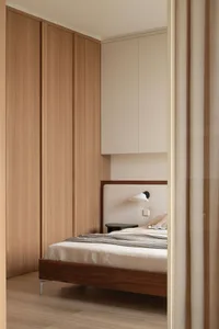Modern minimalist bedroom featuring a dark walnut platform bed with a ribbed upholstered headboard, built-in light wood wardrobes, wall-mounted reading lamp, and neutral beige curtains.